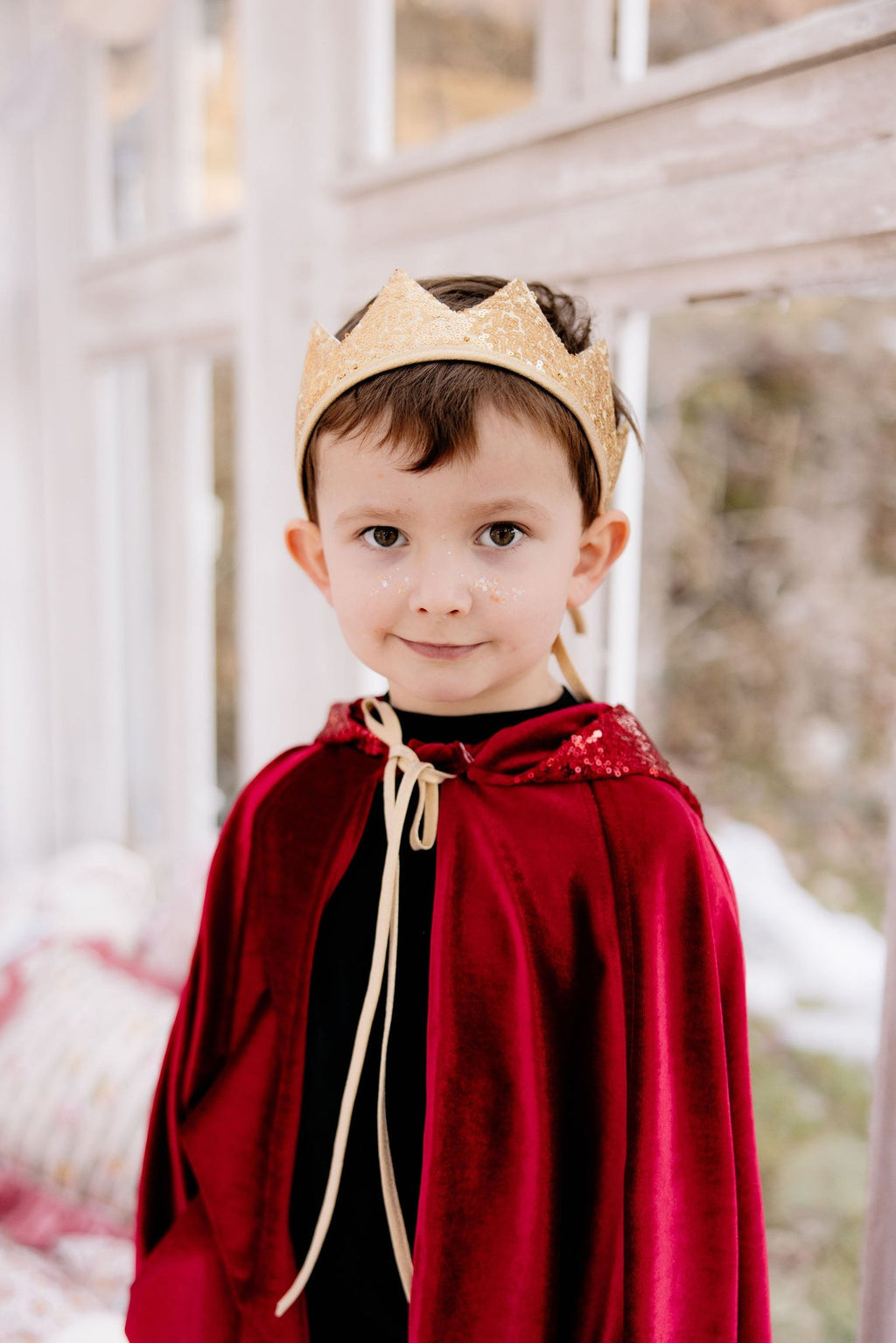 5. Boy wearing a red velour cape and gold crown, standing indoors with a soft background