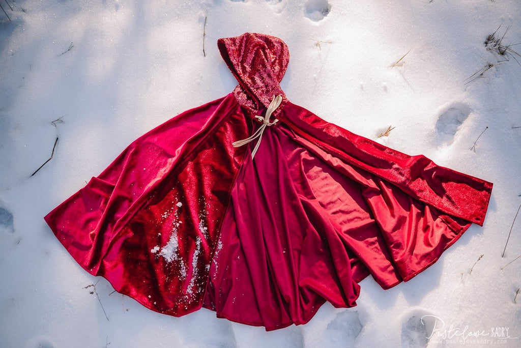 6. Flat lay of red velour cape with hood and laces, displayed on snow