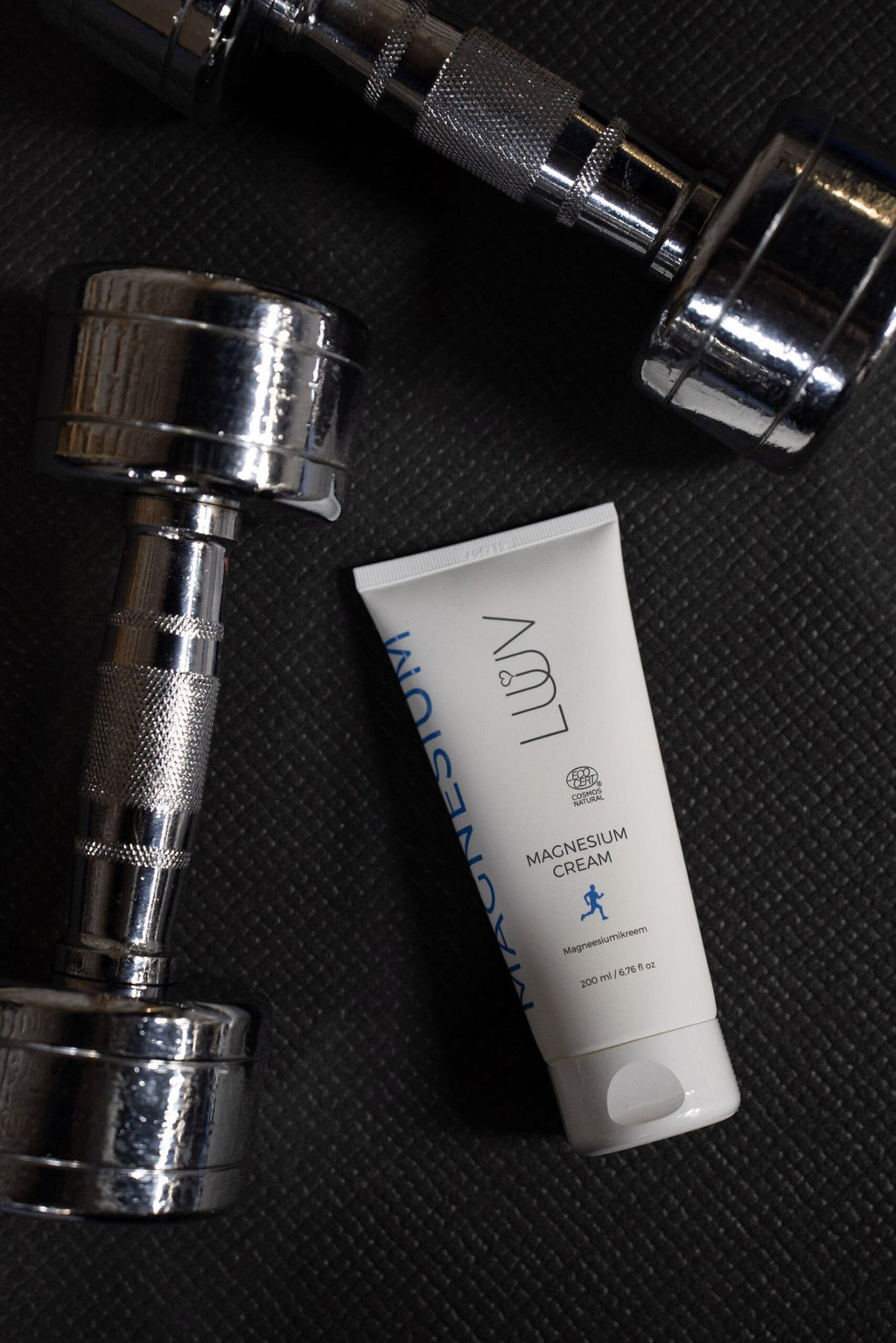 2. LUUV Magnesium Cream placed on gym mat with silver dumbbells