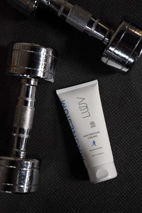 2. LUUV Magnesium Cream placed on gym mat with silver dumbbells