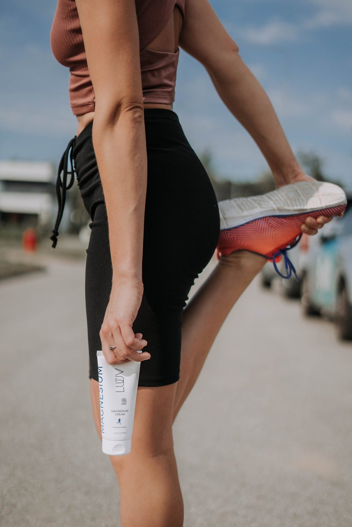 1. Woman in athletic wear stretching leg while holding LUUV Magnesium Cream outdoors