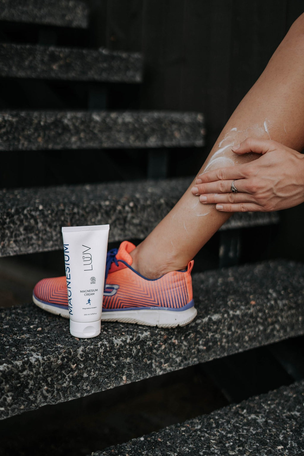 5. Person applying LUUV Magnesium Cream to leg on outdoor steps with colorful sneakers