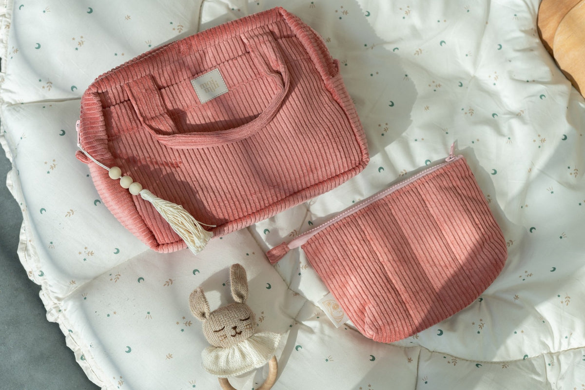 1. Set of two coral makeup bags, one large and one small, on a patterned cushion with a toy