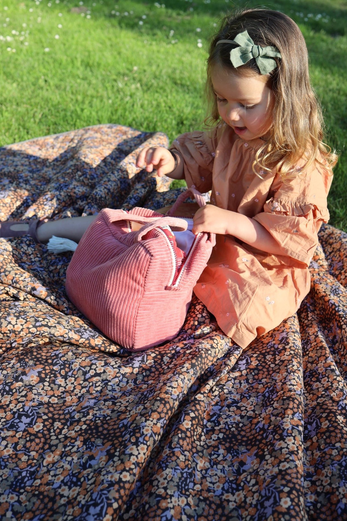 11. Child sitting on floral blanket with coral makeup bag, showcasing outdoor use
