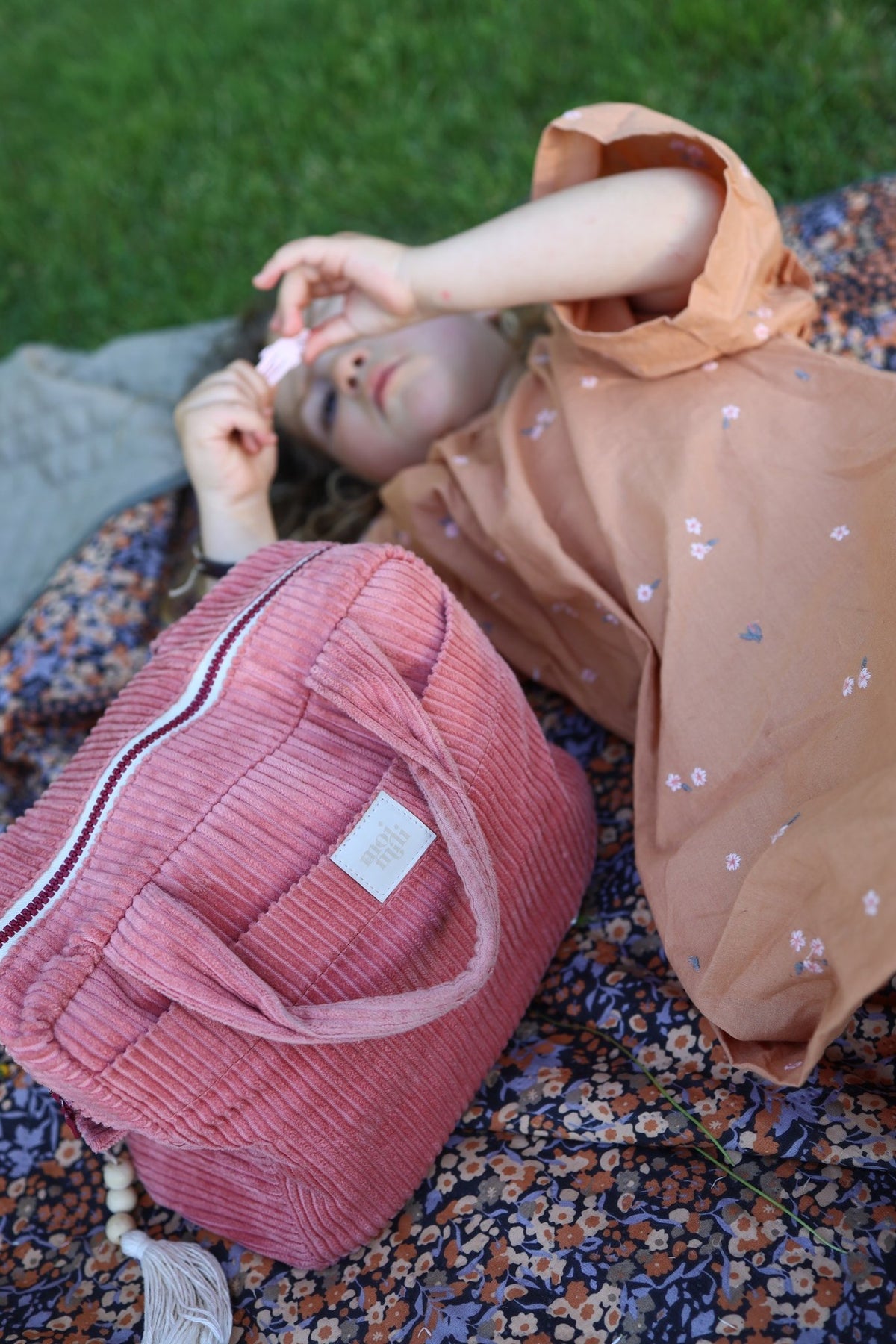 12. Child lying on floral blanket with coral makeup bag, highlighting casual use
