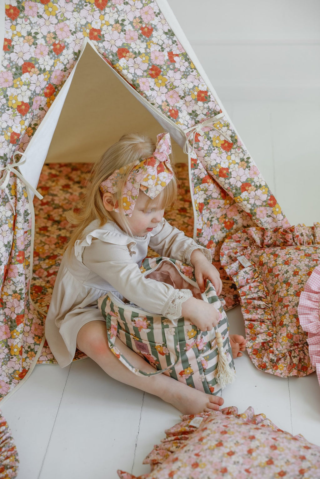 6. Young girl sitting in floral play tent with green striped floral makeup bag, surrounded by matching decor