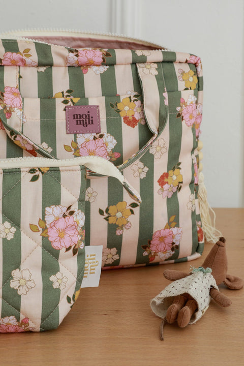 5. Close-up of green striped floral makeup bags with Moi Mili logo on wooden table, featuring small toy