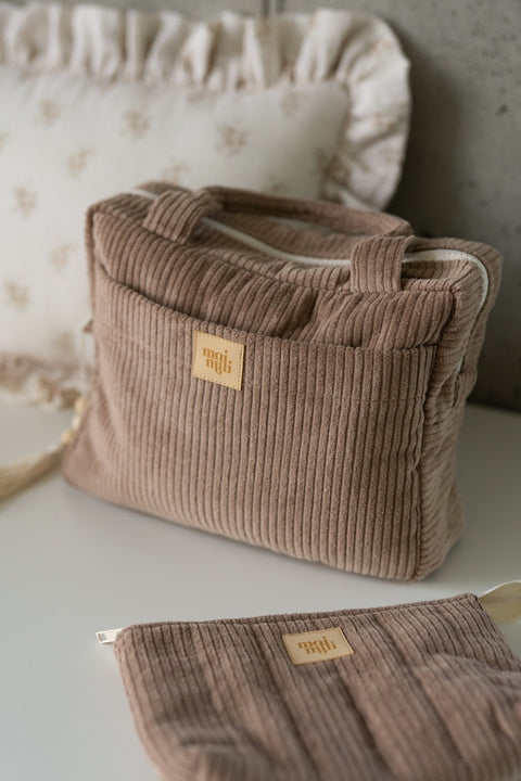 1. Latte-colored makeup bag set of two on a white surface with a decorative pillow in the background, featuring a large and small bag with Moi Mili logo.