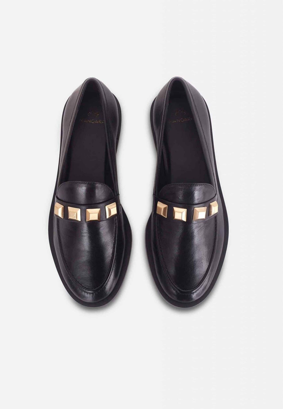 6. Women's black Mangará Caete leather loafers with metal studs, worn by a model lounging on a wooden surface