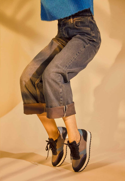 1. Women's Mangará Buriri sneakers in grey, blue, and black worn by a model in a casual setting