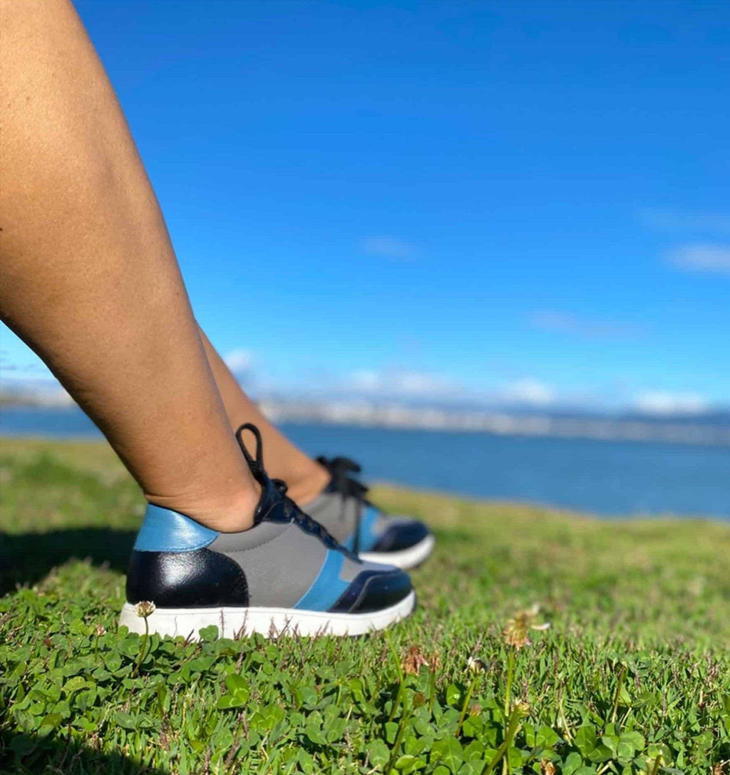 4. Women's Mangará Buriri sneakers in grey, blue, and black shown on grass with lake view