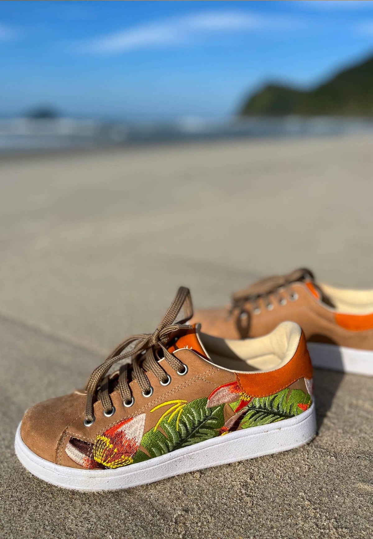 1. Women's Mangará embroidery suede sneakers in brown with floral design, displayed on a beach setting