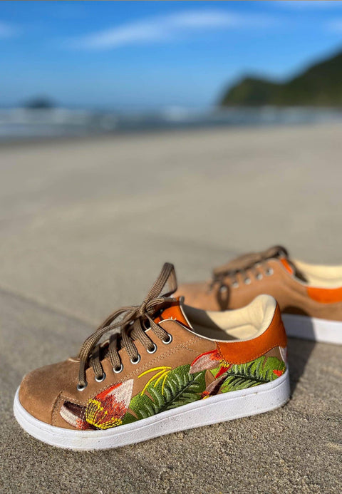 1. Women's Mangará embroidery suede sneakers in brown with floral design, displayed on a beach setting