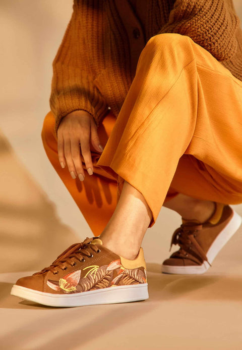 2. Women's Mangará embroidery suede sneakers in brown with floral design, displayed on a beach setting