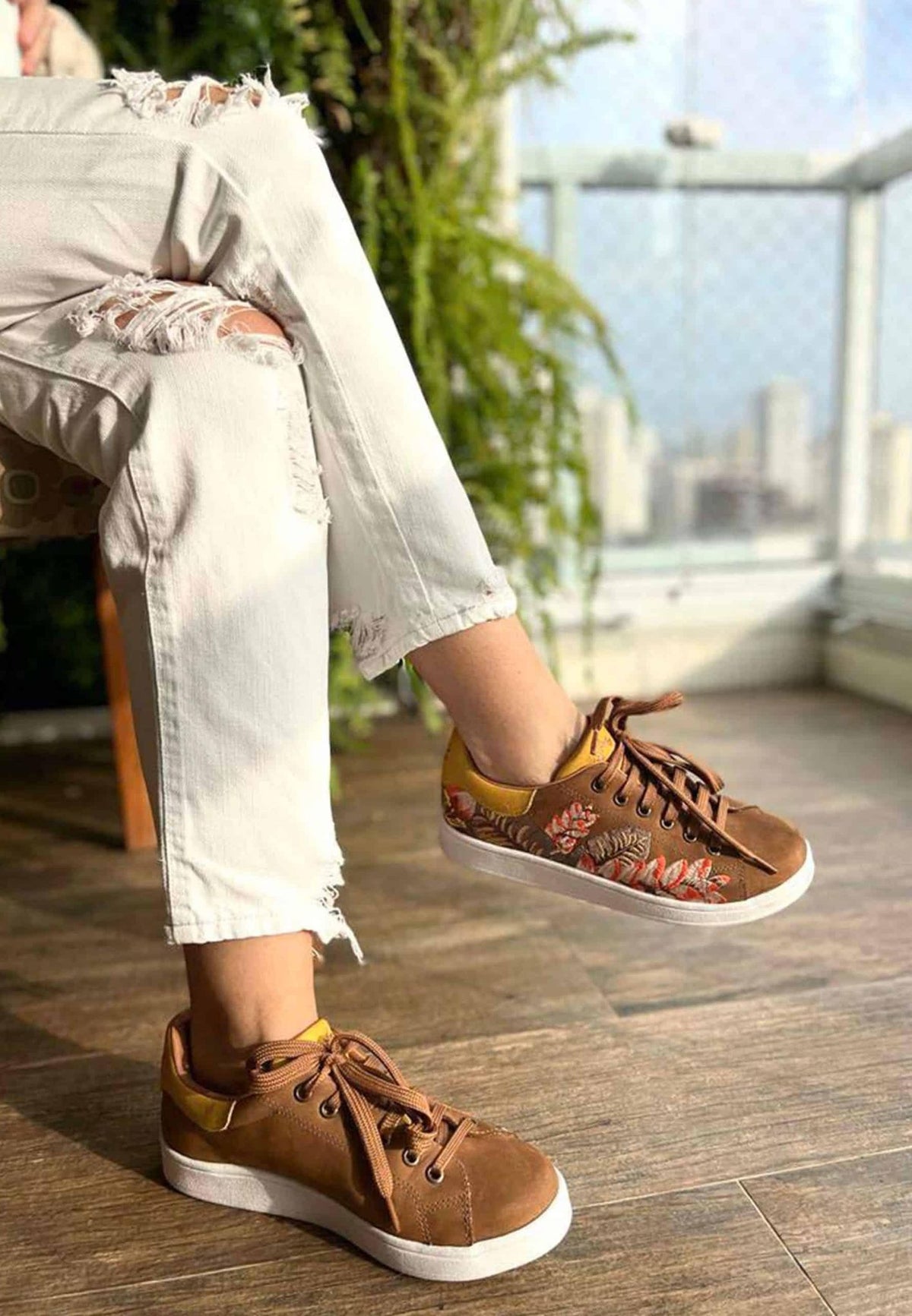 4. Women's Mangará embroidery suede sneakers in brown, paired with white jeans, shown in a casual indoor setting