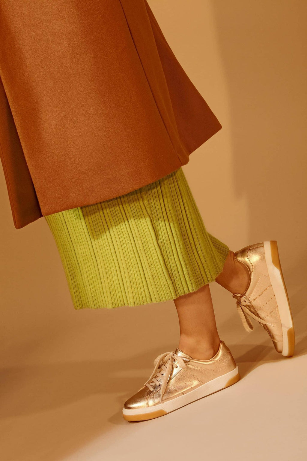 2. Women's Mangará metallic golden sneakers styled with a brown skirt, shown in lifestyle setting