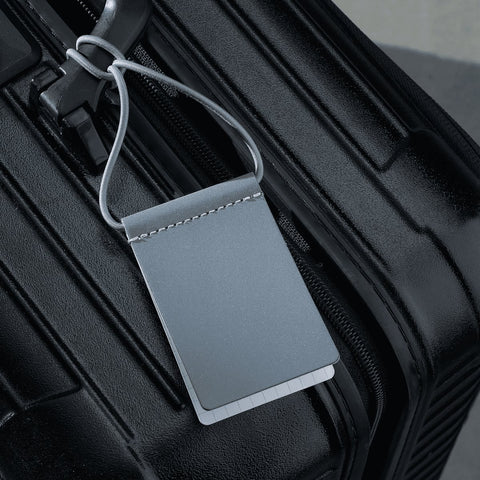 2. Grey MARCH Reflective Luggage Tag attached to black suitcase, highlighting durability