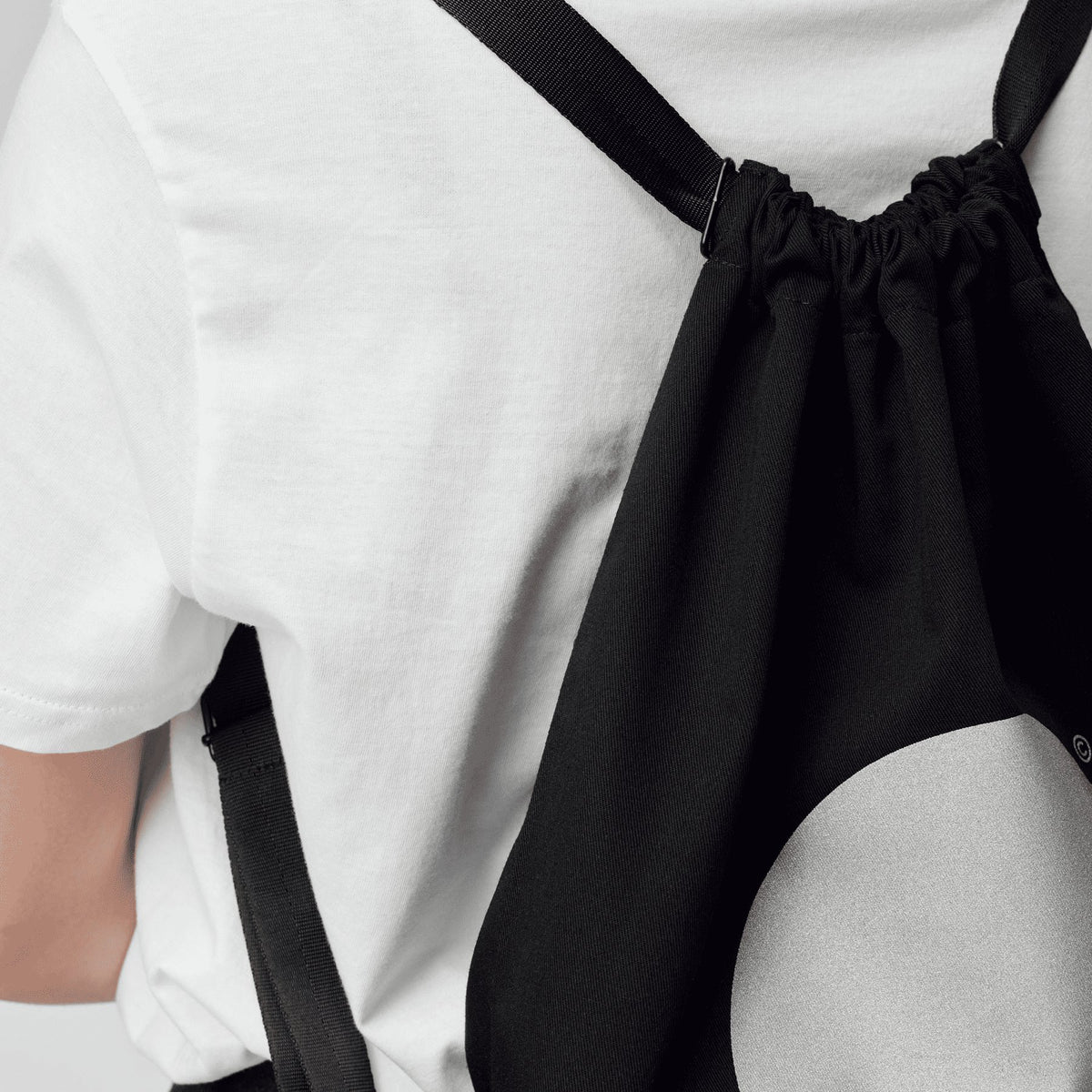 2. Close-up of woman wearing March Design Studio's Water Resistant Reflective Backpack DOT, highlighting reflective circle and drawstring closure