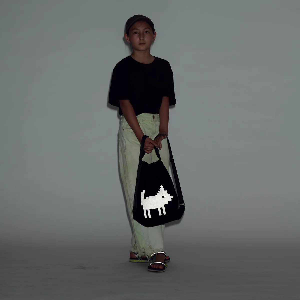 2. Young female model holding March Design Studio's Water Resistant Reflective Backpack DOG, highlighting reflective print in low light