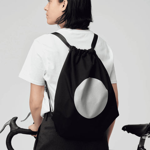 1. Woman wearing March Design Studio's Water Resistant Reflective Backpack DOT while holding a bicycle, showcasing reflective circle design