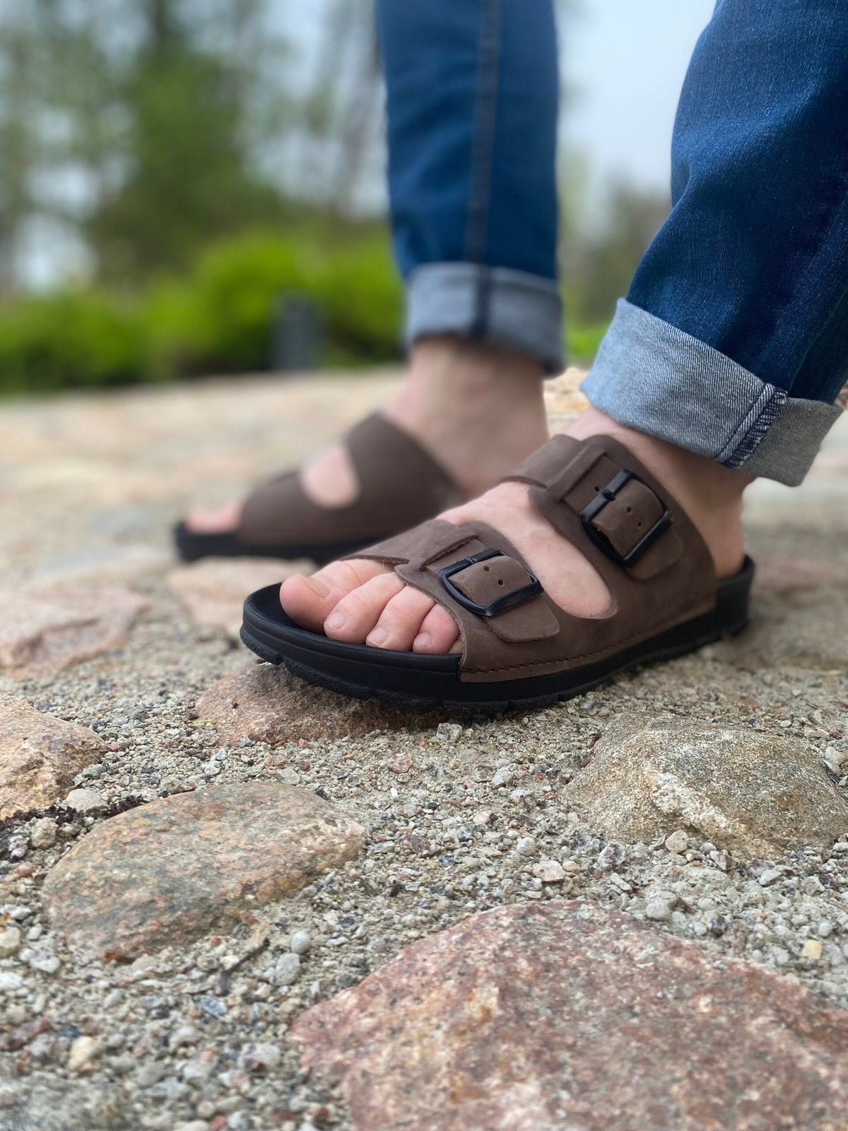 2. Close-up of men's dark brown leather sandals by Omaking on a model walking on rocky terrain