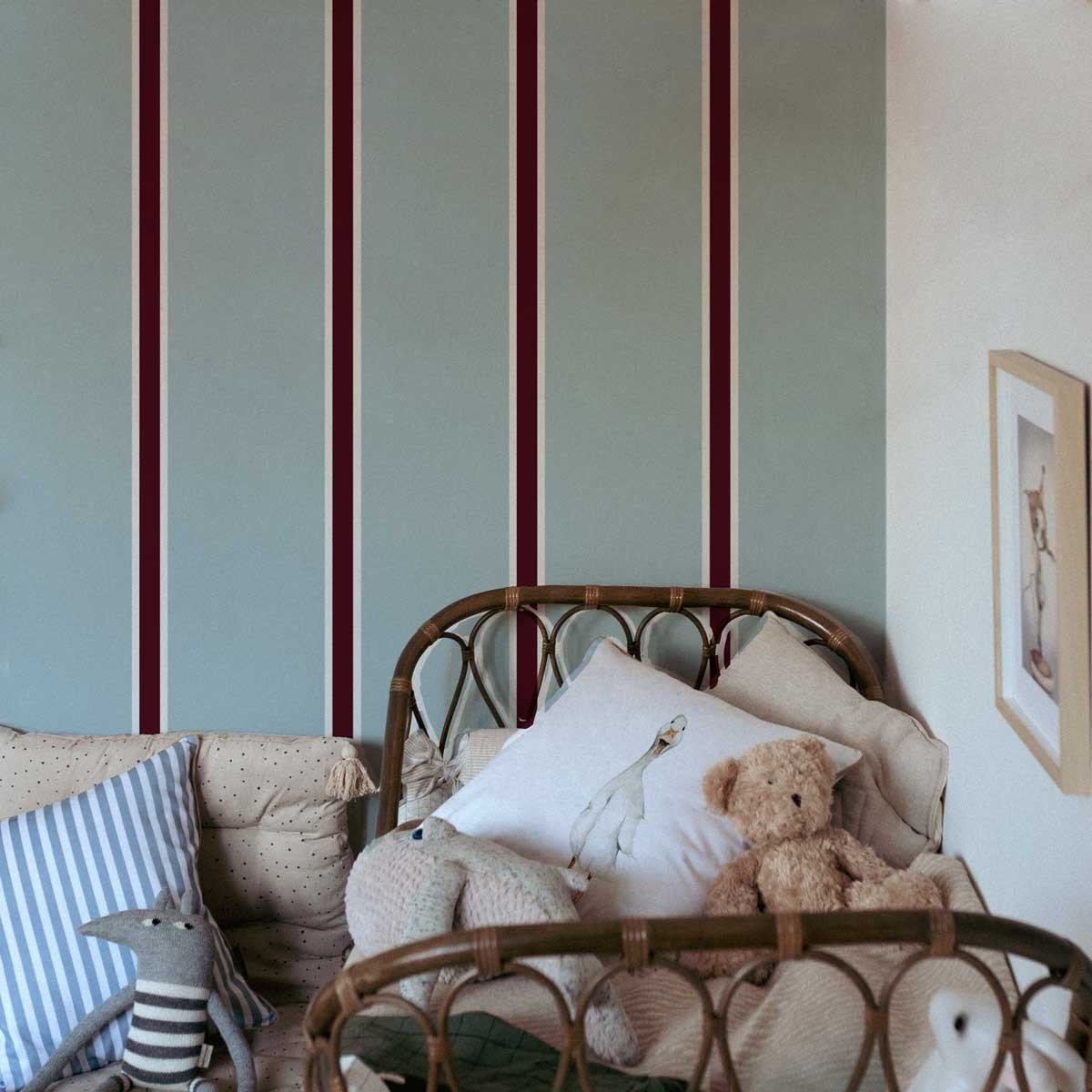 1. Children's room with Maya Stripes Wallpaper featuring wide blue and cherry stripes, rattan crib with plush toys and pillows, creating a cozy and stylish atmosphere