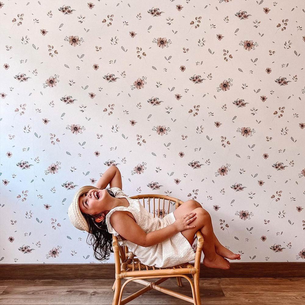 1. Young girl in a white dress and straw hat sitting on a wicker chair against a wall with Dekornik's Flowers Minimini Wallpaper featuring delicate floral patterns