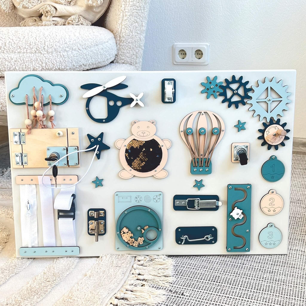 4. Montessori busy board displayed on a rug, featuring blue and beige elements like a bear, gears, and locks, designed for sensory play, by BusyBunnyToys.