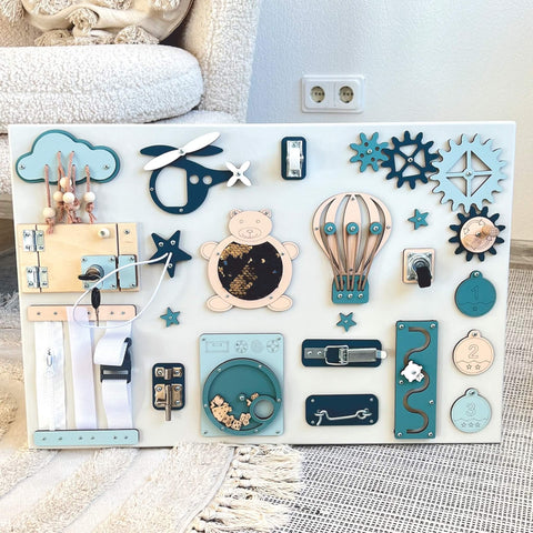 4. Montessori busy board displayed on a rug, featuring blue and beige elements like a bear, gears, and locks, designed for sensory play, by BusyBunnyToys.