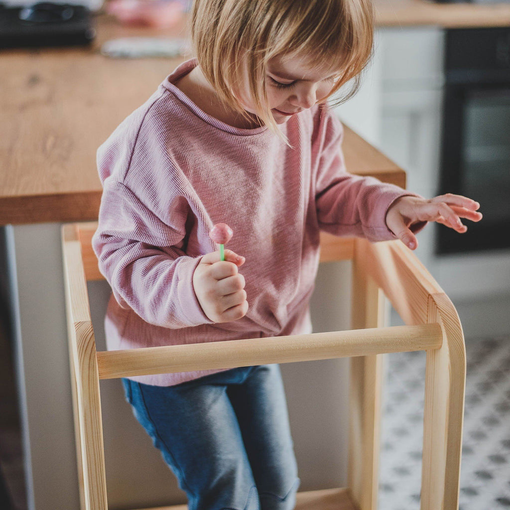 4. Child standing on MeowBaby kitchen helper, holding a toy, in a kitchen setting