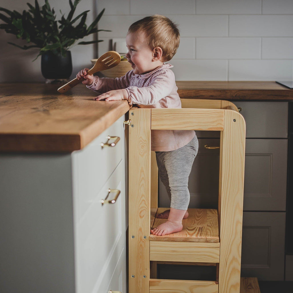 6. Toddler standing on MeowBaby kitchen helper, holding a wooden spoon, in a kitchen environment