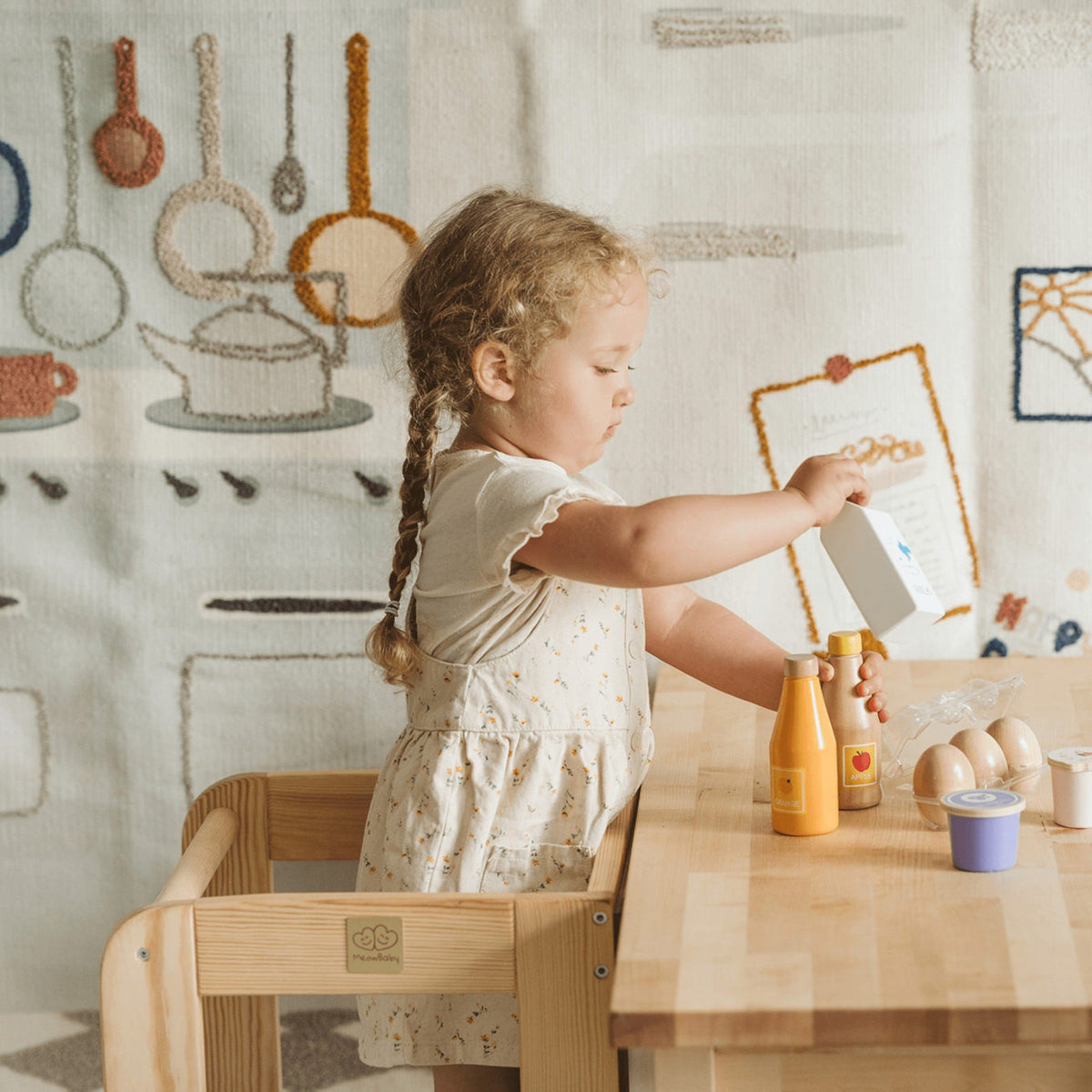 5. Girl using MeowBaby kitchen helper at table, pouring from a carton, in a play kitchen setting
