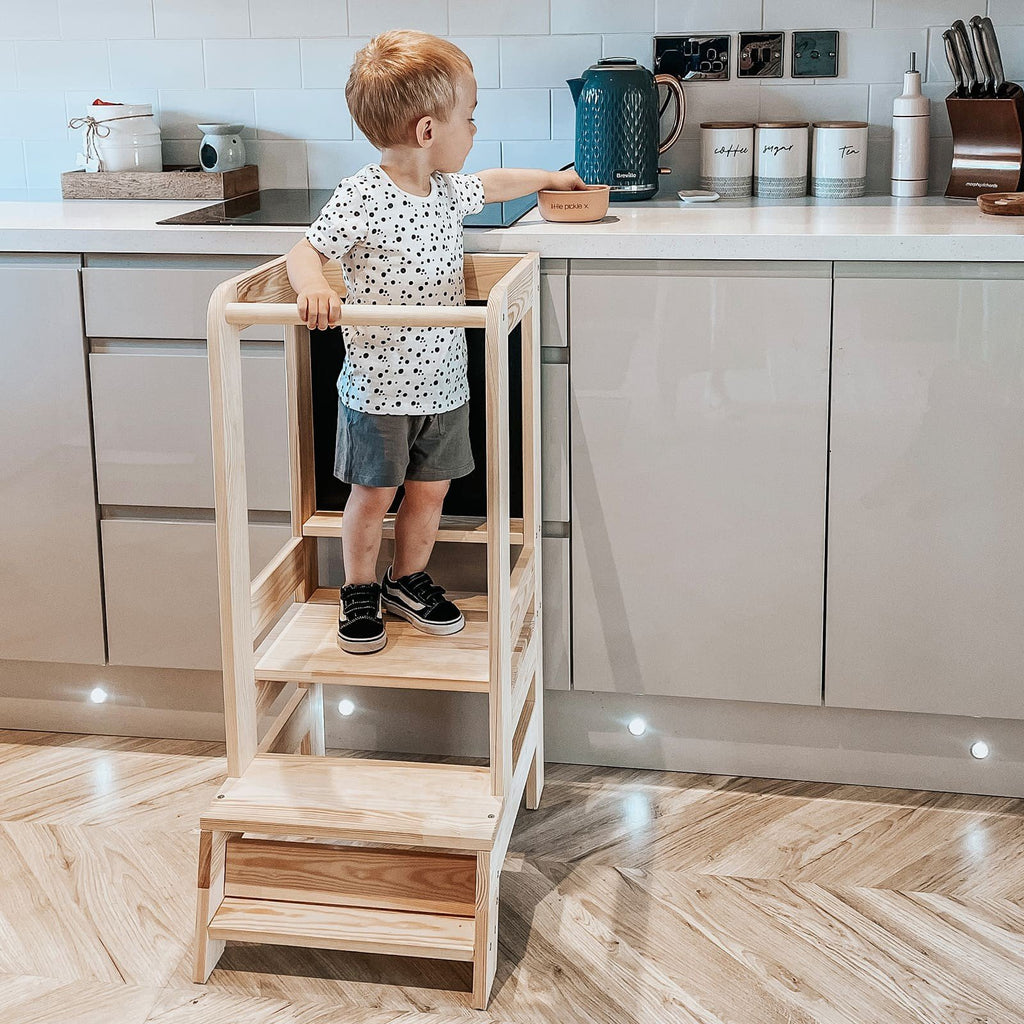 10. Child standing on wooden kitchen helper in modern kitchen environment