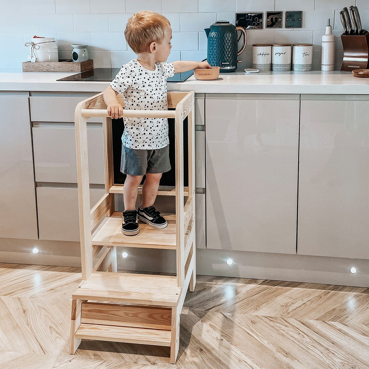 10. Child standing on wooden kitchen helper in modern kitchen environment