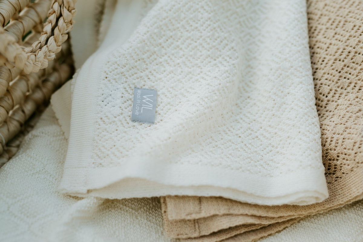 3. Close-up of white merino wool baby blanket with Wool In Love label on textured fabric
