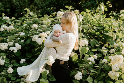 1. Woman holding baby wrapped in white merino wool blanket in garden