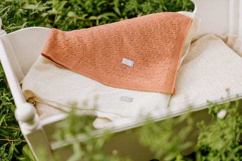 4. Orange merino wool blanket folded on cream blanket in outdoor setting