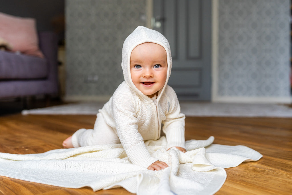 1. Baby in white outfit crawling on merino wool baby blanket in cozy indoor setting