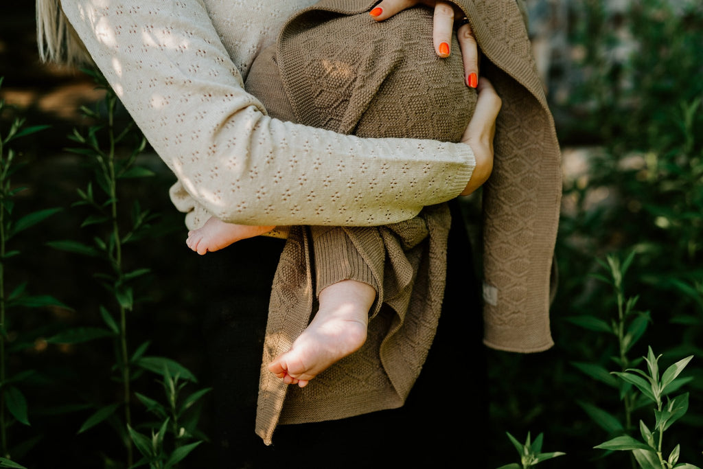 7. Baby wrapped in brown merino wool blanket held by adult in outdoor setting