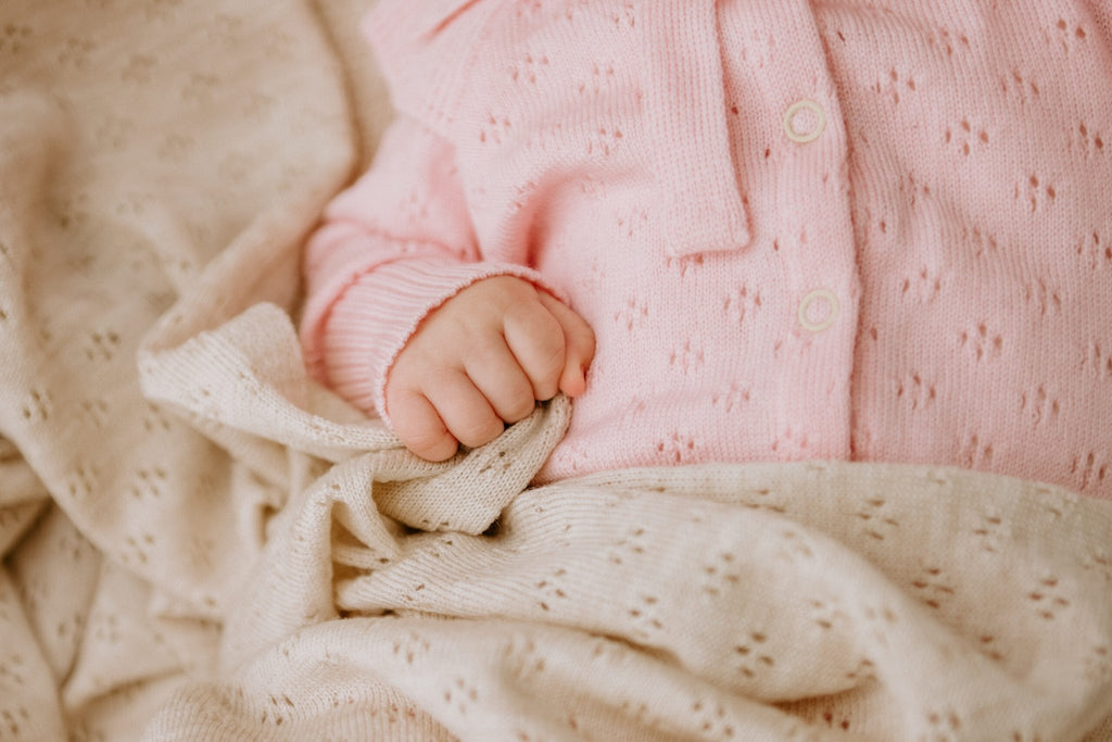 6. Close-up of baby hand holding cream merino wool blanket with floral pattern