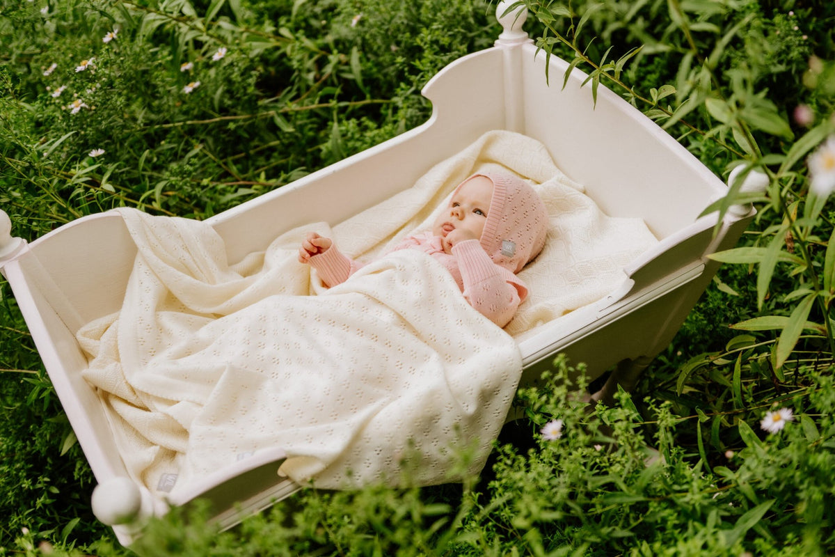 1. Baby wrapped in cream merino wool blanket in a wooden cradle surrounded by greenery