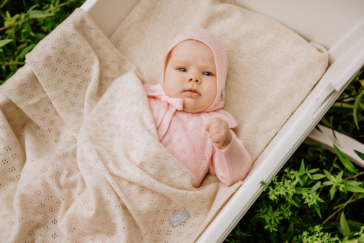 14. Baby in pink outfit wrapped in cream merino wool blanket in white cradle