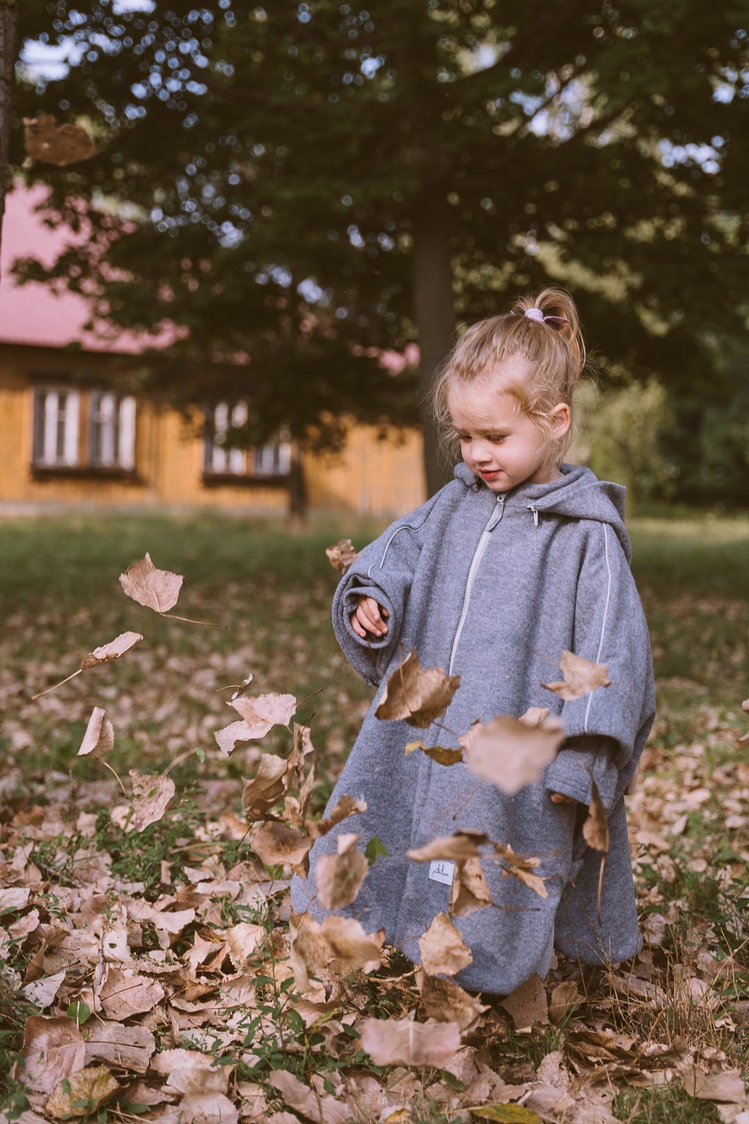 2. Child in grey merino wool poncho playing with leaves in a park