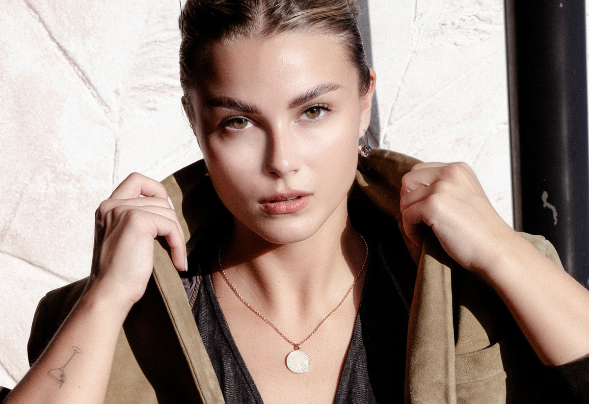 1. Woman wearing MyaMoon Metropolitan Hoops Rolling Charm Earrings with a textured charm, styled with a jacket in a natural setting