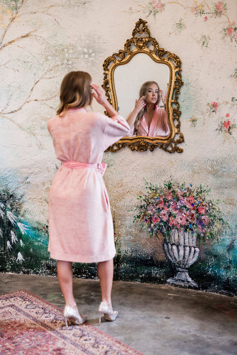 5. Back view of woman in pink bamboo terry robe with shawl collar adjusting hair in front of mirror