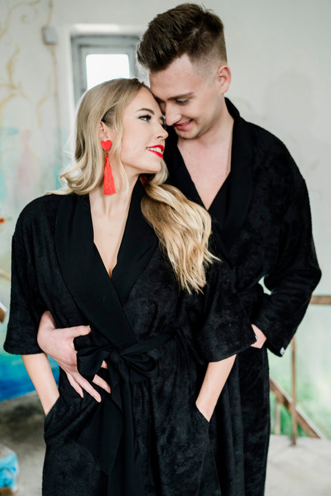 2. Couple wearing matching black bamboo terry robes with shawl collars, woman styled with red earrings