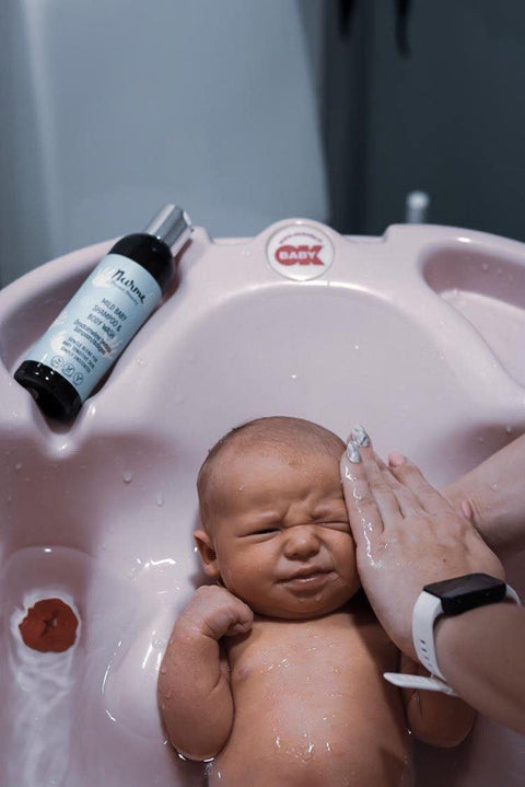 2. Newborn in pink baby bath with Nurme Mild Baby Shampoo & Body Wash bottle on edge