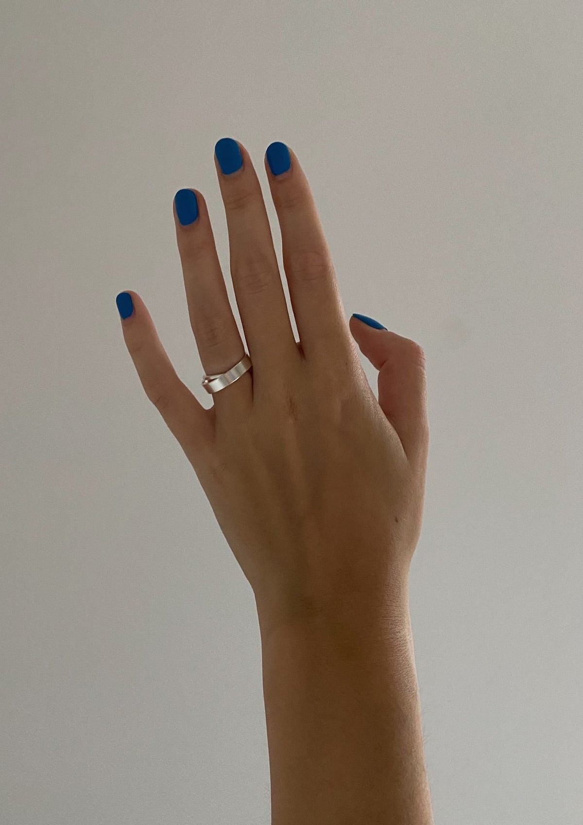 1. Woman's hand with blue nail polish wearing Milky Way ring by NO MORE, against a plain background