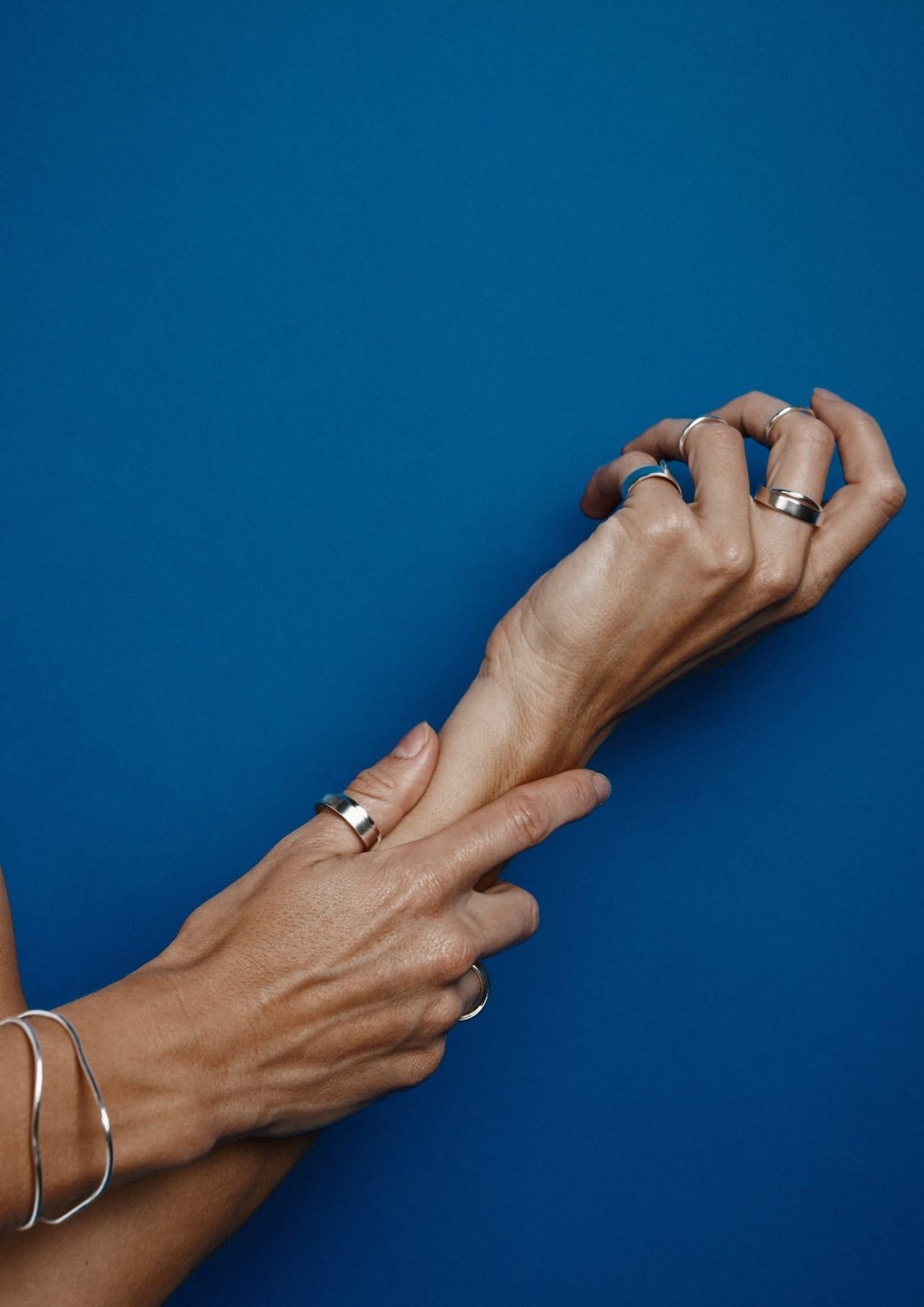 1. Woman's hands adorned with Milky Way ring and other silver jewelry by NO MORE, set against a blue background