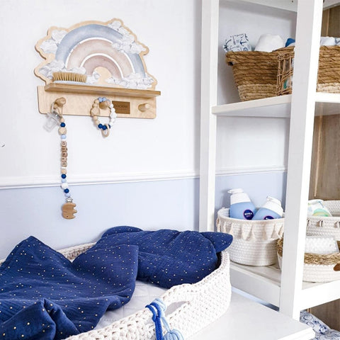 3. Mini wall shelf with blue rainbow design in a nursery setting, holding a brush and hanging accessories